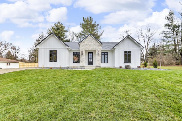 modern inspired farmhouse with fence, a standing seam roof, a front lawn, stone siding, and metal roof