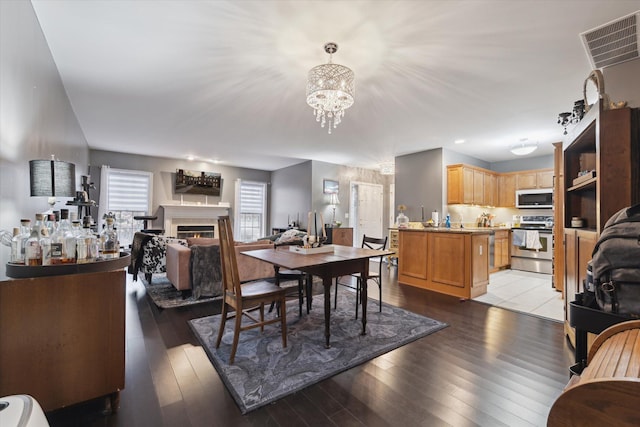 dining room featuring a warm lit fireplace, visible vents, light wood finished floors, and an inviting chandelier