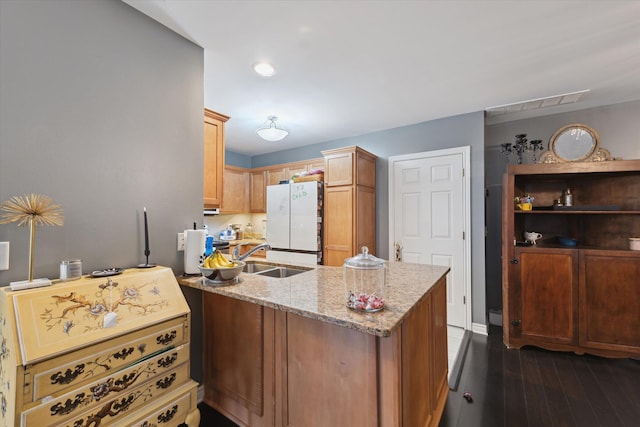 kitchen with light stone counters, dark wood-style flooring, freestanding refrigerator, a peninsula, and a sink