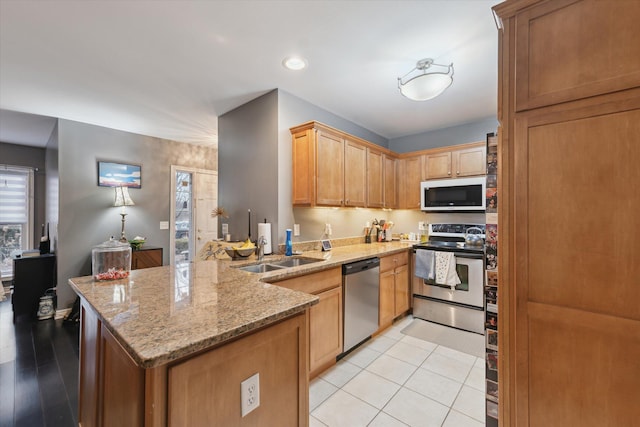 kitchen with light stone counters, light tile patterned flooring, a peninsula, a sink, and appliances with stainless steel finishes