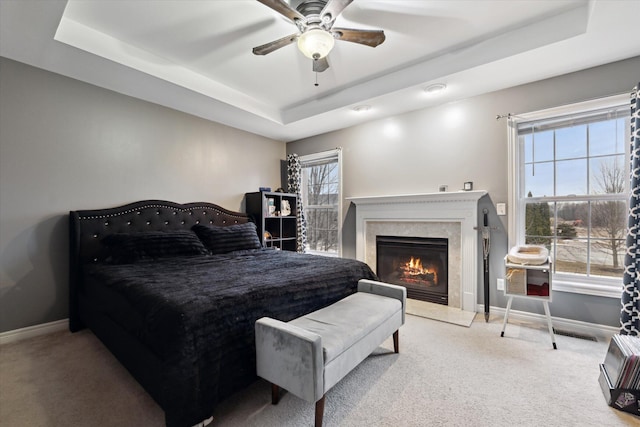 carpeted bedroom with a high end fireplace, a tray ceiling, baseboards, and a ceiling fan