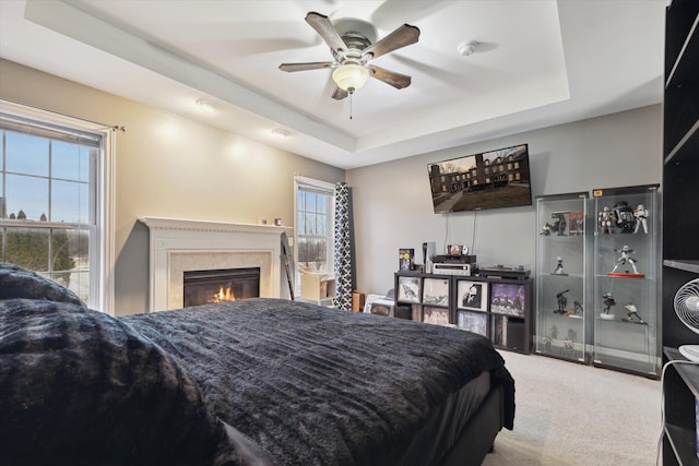 bedroom with ceiling fan, a tray ceiling, carpet, and a high end fireplace