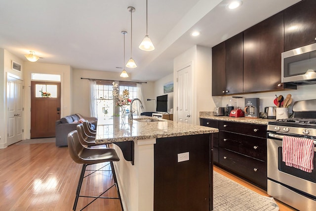 kitchen featuring open floor plan, a kitchen breakfast bar, stainless steel appliances, light wood-style floors, and a sink