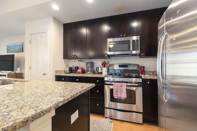 kitchen featuring light stone counters, stainless steel appliances, recessed lighting, a sink, and light wood-type flooring