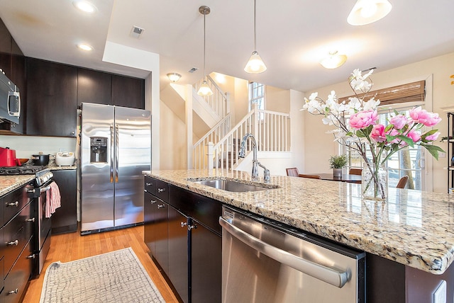 kitchen featuring stainless steel appliances, a sink, hanging light fixtures, light stone countertops, and light wood finished floors