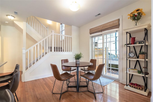 dining space with stairs, hardwood / wood-style floors, visible vents, and baseboards