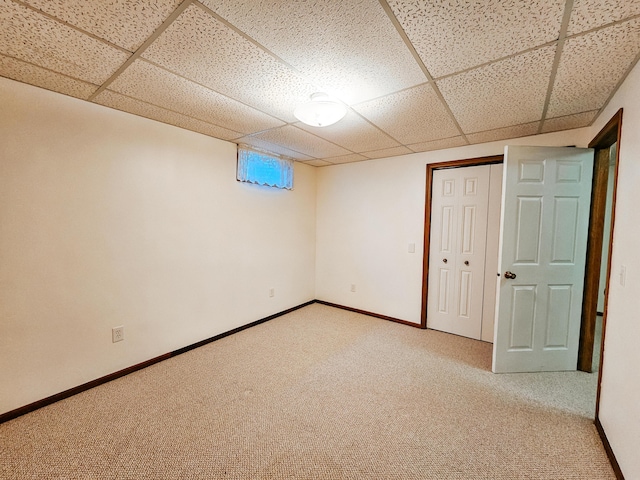 basement featuring a drop ceiling, carpet flooring, and baseboards