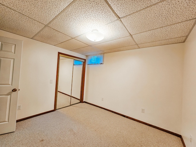 unfurnished bedroom featuring a closet, carpet, a paneled ceiling, and baseboards