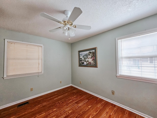 spare room with visible vents, a textured ceiling, baseboards, and wood finished floors