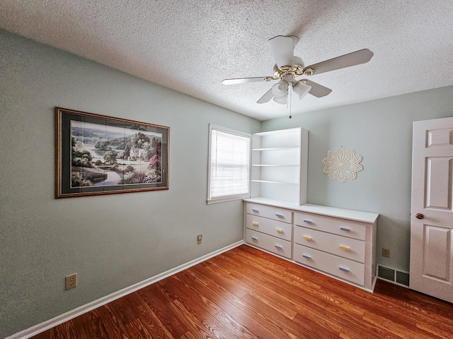 unfurnished bedroom with visible vents, a ceiling fan, a textured ceiling, wood finished floors, and baseboards