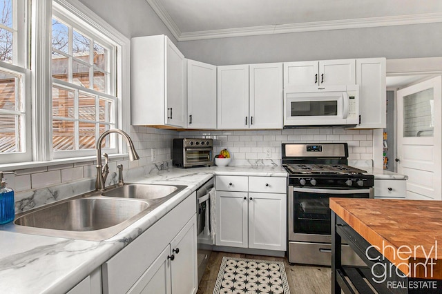 kitchen featuring appliances with stainless steel finishes, white cabinets, crown molding, and a sink