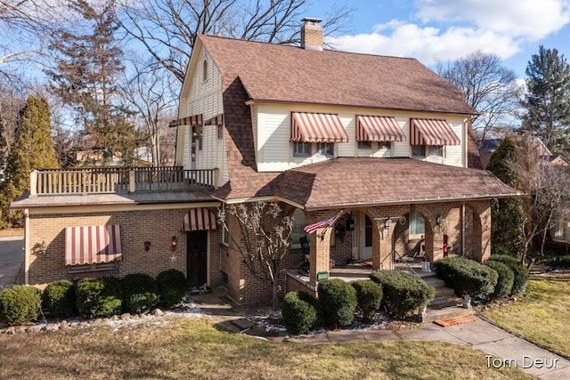 view of front of house with a shingled roof, a balcony, a chimney, covered porch, and brick siding