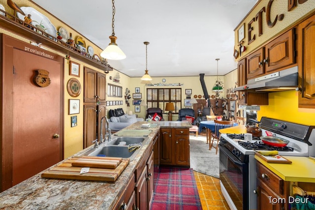 kitchen featuring open floor plan, under cabinet range hood, pendant lighting, a sink, and gas stove