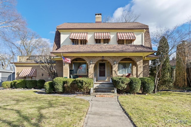 view of front of home with a porch, a front yard, brick siding, and a chimney