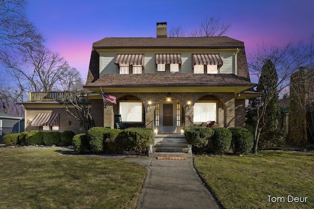 view of front of home featuring a front lawn, roof with shingles, a porch, and brick siding