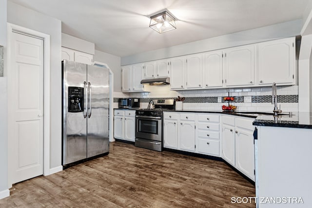 kitchen featuring dark wood-style flooring, dark countertops, appliances with stainless steel finishes, a sink, and under cabinet range hood