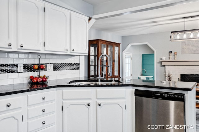 kitchen with tasteful backsplash, white cabinets, dishwasher, a brick fireplace, and a sink