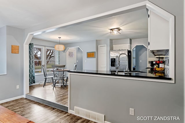 kitchen featuring visible vents, arched walkways, stainless steel fridge with ice dispenser, dark countertops, and a peninsula