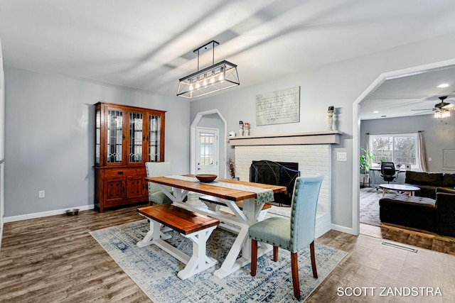 dining room with arched walkways, a fireplace, wood finished floors, and baseboards