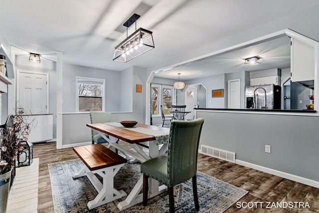 dining room with arched walkways, visible vents, plenty of natural light, and wood finished floors