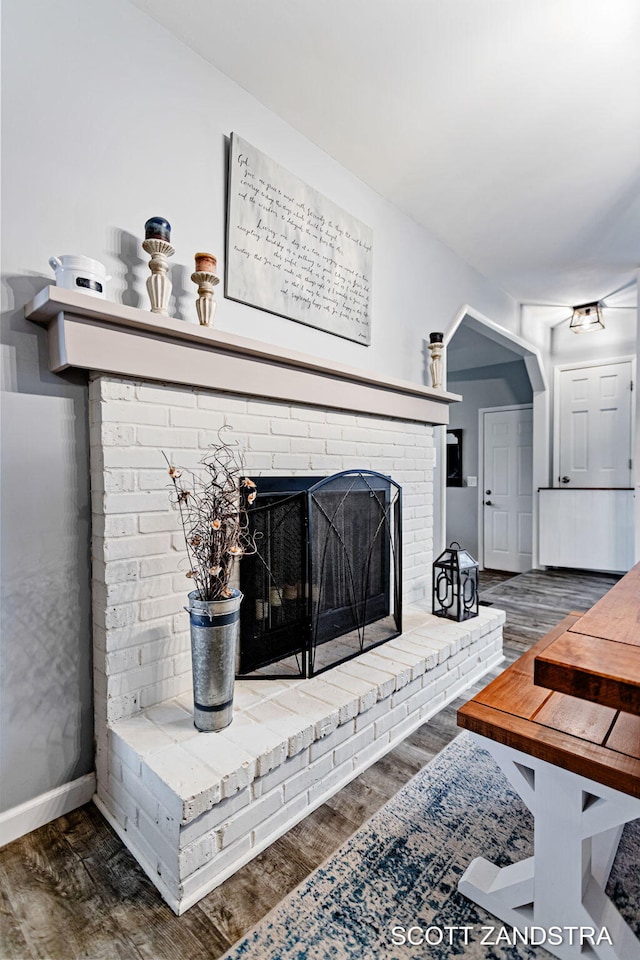 living area featuring a brick fireplace, baseboards, arched walkways, and wood finished floors