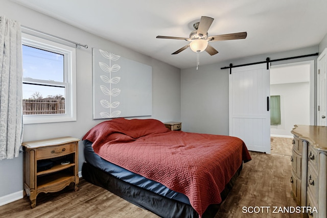 bedroom with wood finished floors, ceiling fan, baseboards, and a barn door