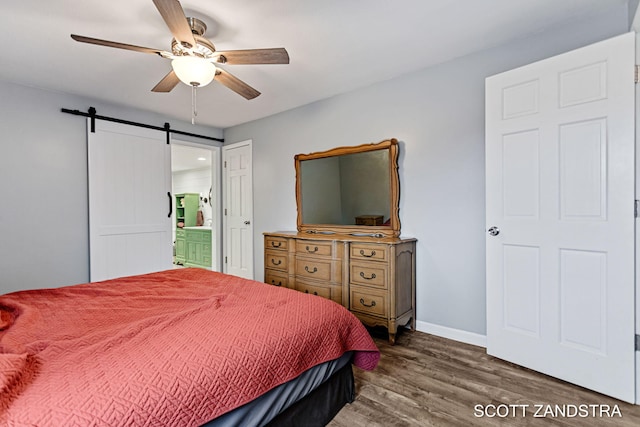 bedroom featuring ensuite bathroom, a barn door, ceiling fan, wood finished floors, and baseboards