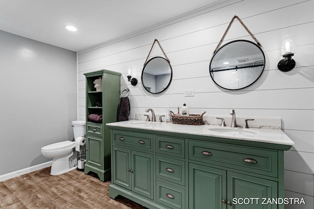 bathroom featuring toilet, double vanity, a sink, and wood finished floors