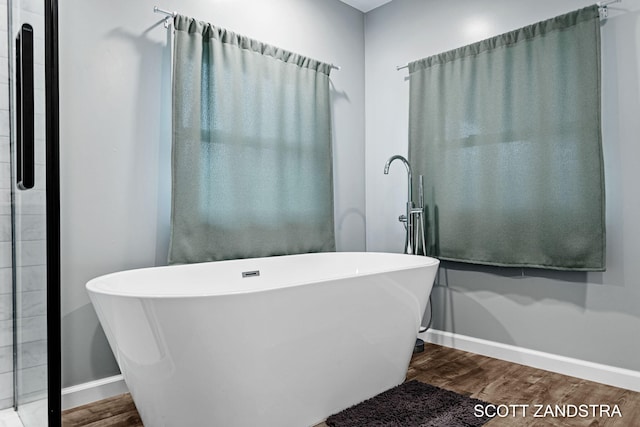 bathroom with a freestanding tub, baseboards, and wood finished floors