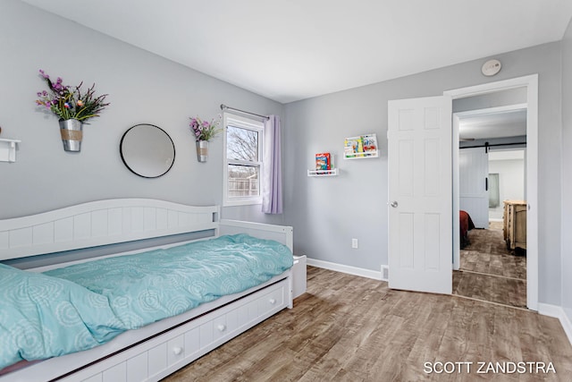 bedroom with wood finished floors, baseboards, and a barn door