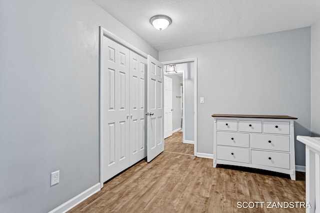 unfurnished bedroom with a closet, baseboards, a textured ceiling, and light wood finished floors