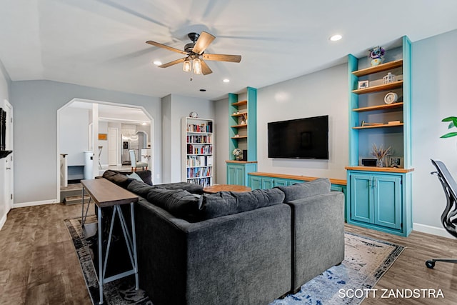 living area featuring arched walkways, wood finished floors, a ceiling fan, built in features, and baseboards