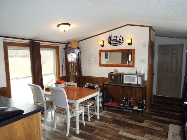 dining space featuring lofted ceiling, dark wood-style floors, ornamental molding, and wainscoting