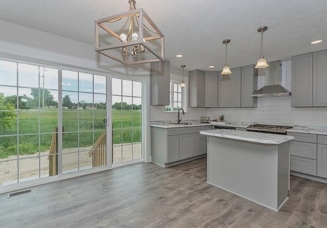 kitchen featuring gray cabinetry, a sink, visible vents, wall chimney range hood, and backsplash