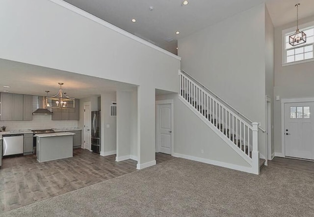 unfurnished living room featuring baseboards, stairway, carpet, a high ceiling, and a chandelier