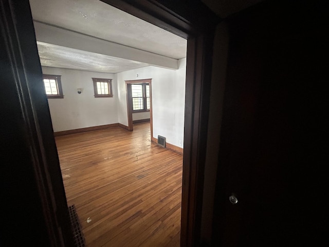 empty room featuring plenty of natural light, baseboards, visible vents, and wood finished floors