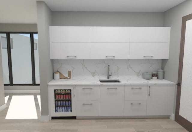 bar featuring light wood-style flooring, a sink, backsplash, and baseboards