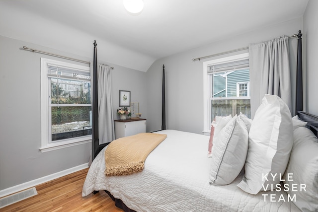 bedroom with wood finished floors, visible vents, vaulted ceiling, and multiple windows