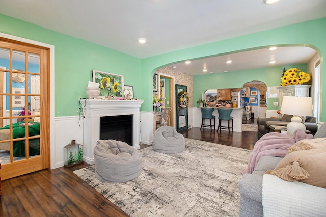 living room with arched walkways, wainscoting, a fireplace, and wood finished floors