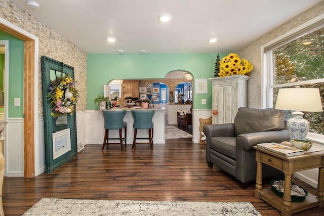 living area with dark wood-type flooring, arched walkways, a wainscoted wall, and recessed lighting