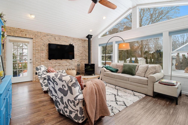 sunroom / solarium with lofted ceiling, plenty of natural light, a wood stove, and a ceiling fan