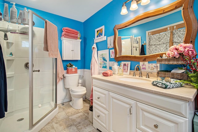 bathroom featuring toilet, a stall shower, vanity, and a wainscoted wall