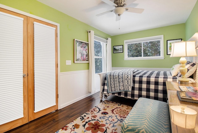 bedroom with a wainscoted wall, dark wood-style floors, and a ceiling fan