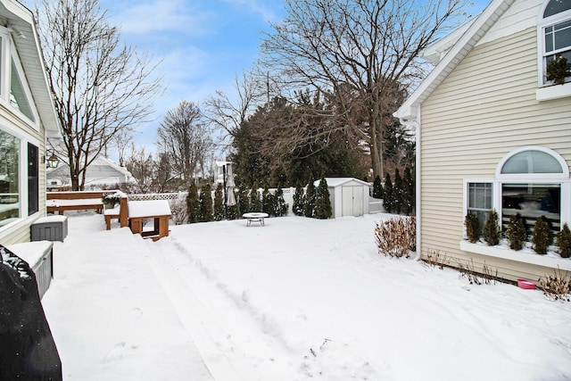 snowy yard featuring an outdoor structure, a storage shed, and fence