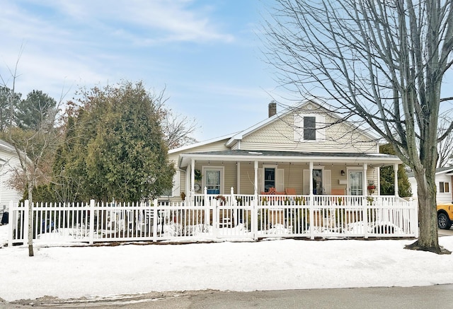 view of front facade featuring covered porch, a fenced front yard, and a chimney