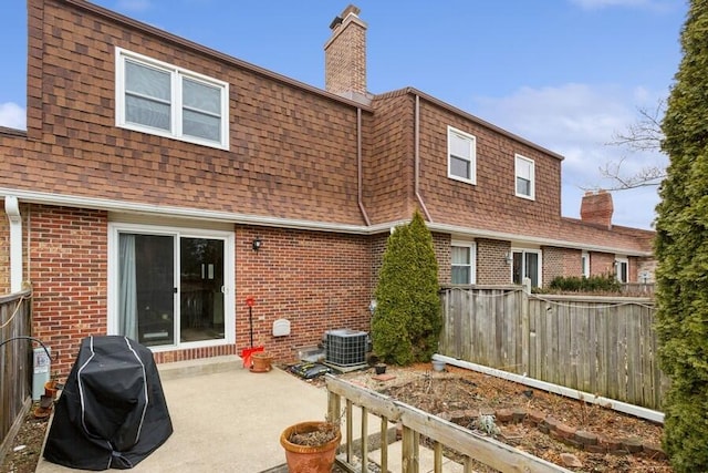 back of property featuring a patio area, a chimney, brick siding, and roof with shingles