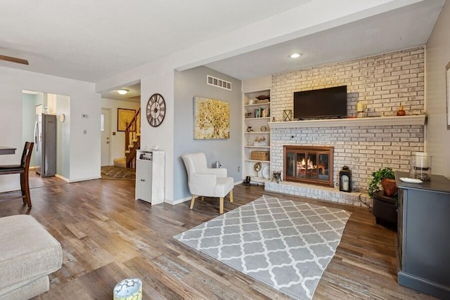 living room with a fireplace, wood finished floors, visible vents, built in features, and stairs