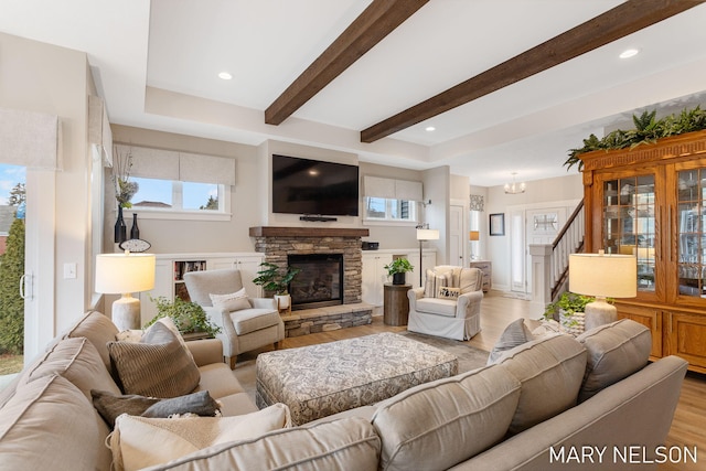 living area with a fireplace, beam ceiling, plenty of natural light, and light wood-style floors