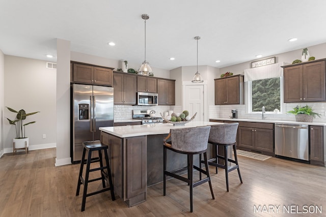 kitchen with dark brown cabinetry, appliances with stainless steel finishes, light countertops, and a kitchen bar