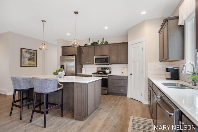 kitchen with a sink, stainless steel appliances, dark brown cabinets, light wood-style floors, and a center island